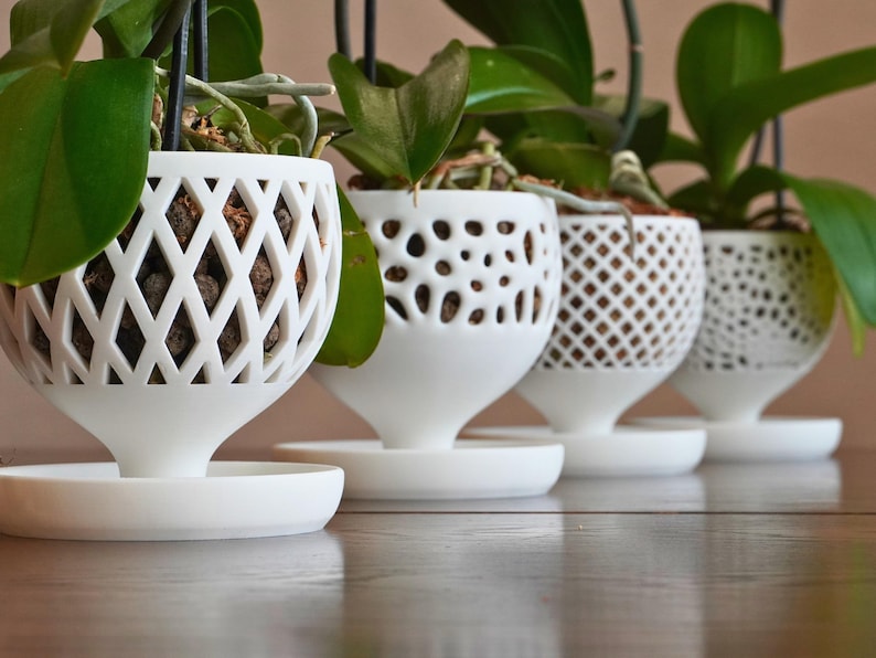 May include: Four white ceramic orchid pots with different patterned designs. The pots are hanging from the ceiling and have a saucer underneath.