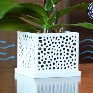 May include: A white square plant pot with a perforated design, holding a green plant. The pot sits on a matching square base. The image includes the text "INSPIRED DESIGNED MADE IN THE USA".