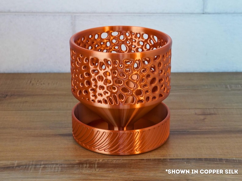 May include: A copper-colored planter with a geometric pattern and a textured base. The planter is designed for indoor plants and has a drainage system.