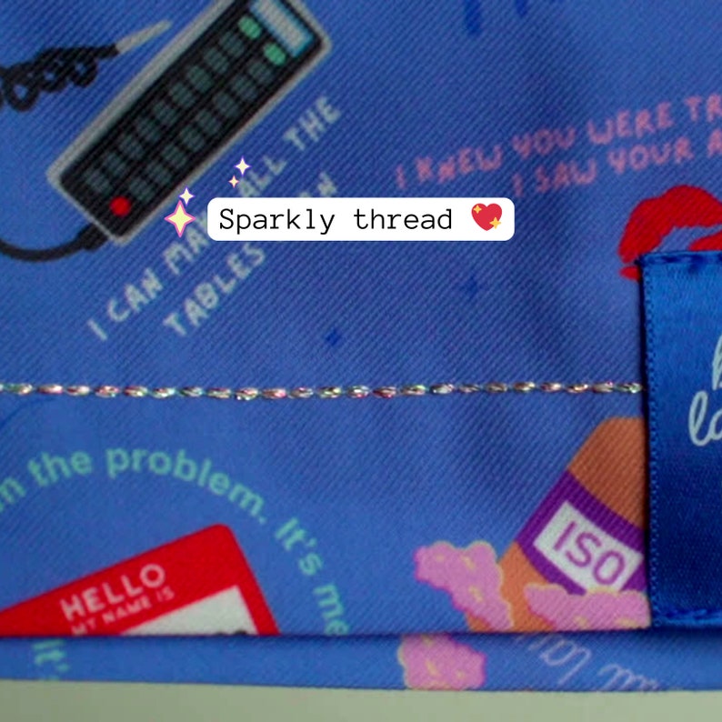 May include: Close-up of a blue fabric with various printed elements, including a remote control, text, and a name tag. A sparkly thread runs horizontally across the fabric. The text "Sparkly thread" is also visible.
