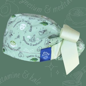Puede incluir: Un gorro quir&uacute;rgico verde claro con un lazo blanco. El gorro est&aacute; estampado con peque&ntilde;as ilustraciones en blanco y negro de tazas de caf&eacute;, aguacates y posturas de yoga. Una etiqueta azul dice "blue laundry".