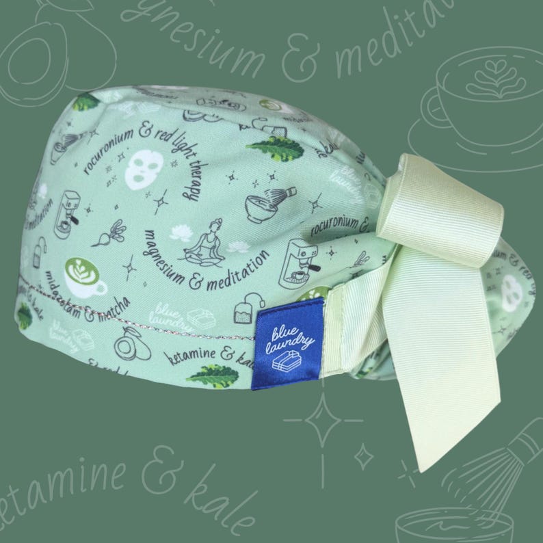 Puede incluir: Un gorro quir&uacute;rgico verde claro con un lazo blanco. El gorro est&aacute; estampado con peque&ntilde;as ilustraciones en blanco y negro de tazas de caf&eacute;, aguacates y posturas de yoga. Una etiqueta azul dice "blue laundry".