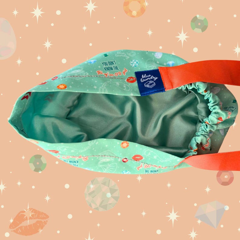 May include: A turquoise drawstring bag with an orange strap. The bag's exterior features a pattern of lips, donuts, and text that reads "You Don't Know The F*ck Or Girl". The interior is a solid teal color, and a blue label reads "Blue Laundry".