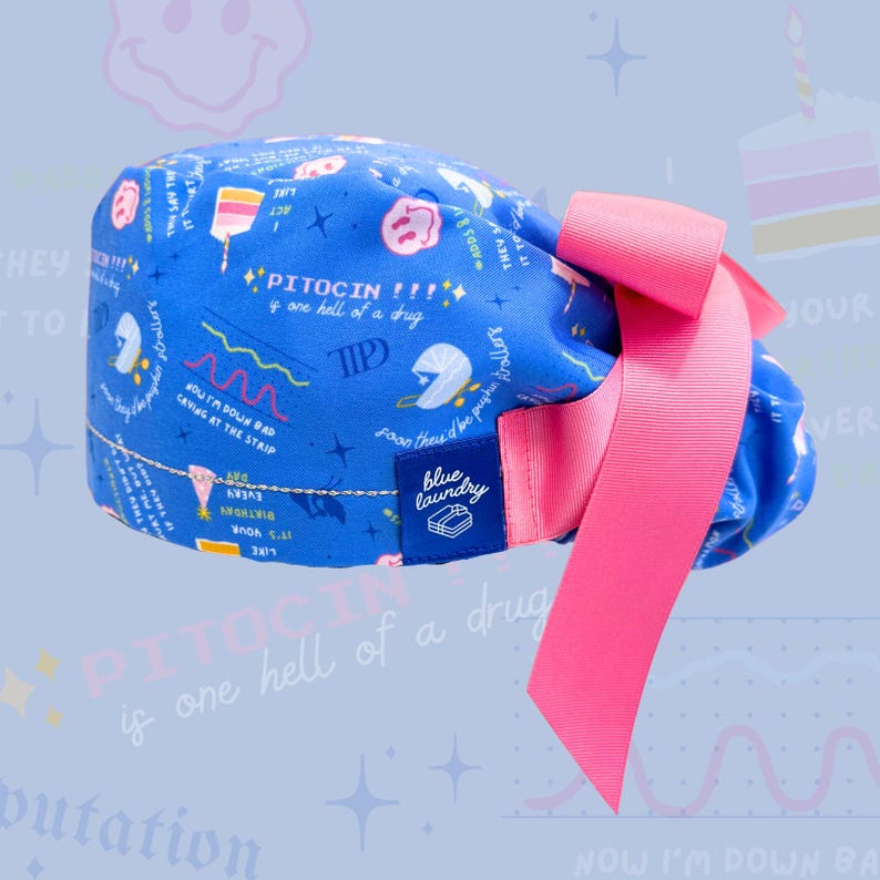 May include: Blue and pink surgical scrub hat with a bow. The hat has a print of medical-related text and illustrations. The text includes "Pitocin is one hell of a drug" and "Blue Laundry".