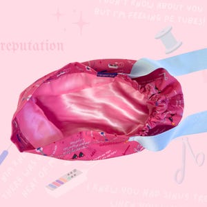 May include: A pink satin-lined bouffant scrub cap with a light blue elastic band. The cap features a repeating pattern of medical-themed illustrations and text. The interior is a solid pink color.