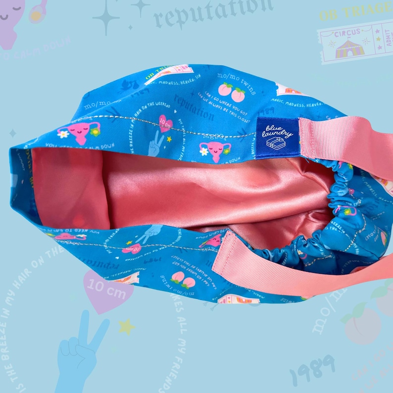 May include: A blue and pink surgical scrub hat with a variety of colorful illustrations and text, including "reputation", "mo/mo twin", "10 cm", and "Blue Laundry".