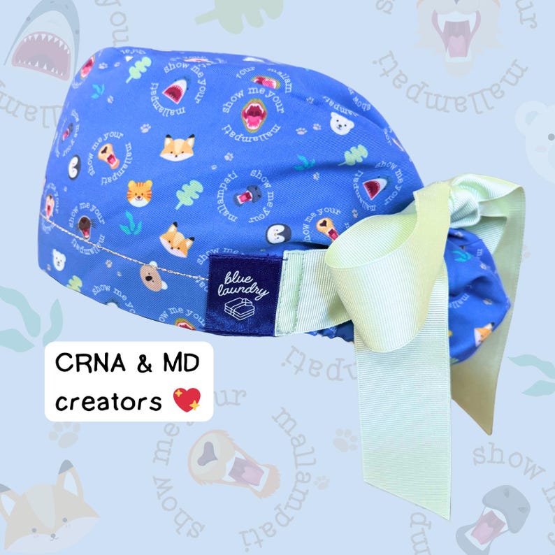 Puede incluir: Un gorro quir&uacute;rgico azul con un lazo verde claro. El gorro tiene un estampado de animales de dibujos animados y las palabras "show me your mallampati". La etiqueta dice "blue laundry". El texto de la imagen dice "CRNA & MD creators".