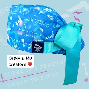 May include: A blue surgical scrub cap with a teal bow. The cap features medical-themed graphics and text, including "What's the blood pressure right now?" and "There is a fracture. I need to fix it."