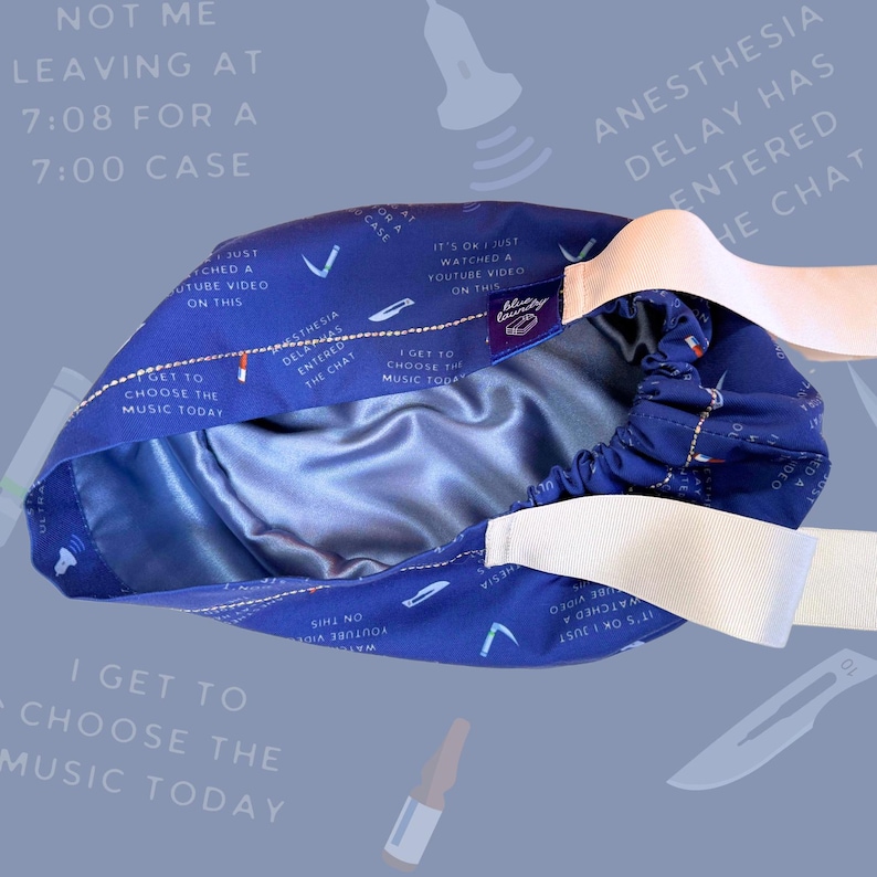 May include: A blue surgical cap with white elastic straps. The cap has a satin lining and features a repeating pattern of text and images, including "I get to choose the music today" and "Anesthesia delay has entered the chat".