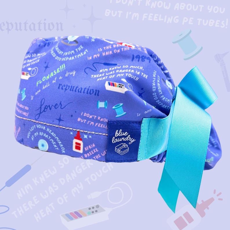 May include: A blue scrub cap with a light blue bow. The cap features a pattern of text and small illustrations in white and blue. The text includes the words "reputation" and "Lover". A blue label reads "blue laundry".