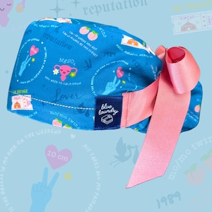 May include: A blue scrub cap with a pink bow. The cap features various graphics, including peaches, hearts, and text like "reputation" and "Lover." A pink heart graphic shows "10 cm."
