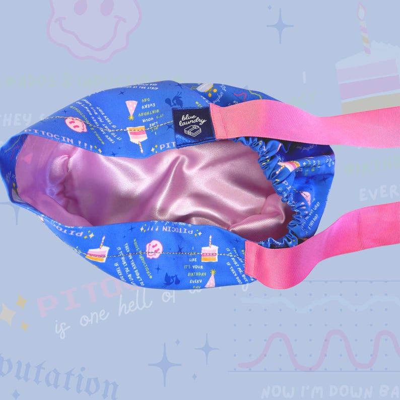 K&ouml;nnte beinhalten: Ein blaues Satin-Haargummi mit einem rosa Band. Das Haargummi hat ein Geburtstagstortenmuster mit dem Text "PITOCIN!!" und "Es ist jeden Tag dein Geburtstag!" darauf gedruckt.