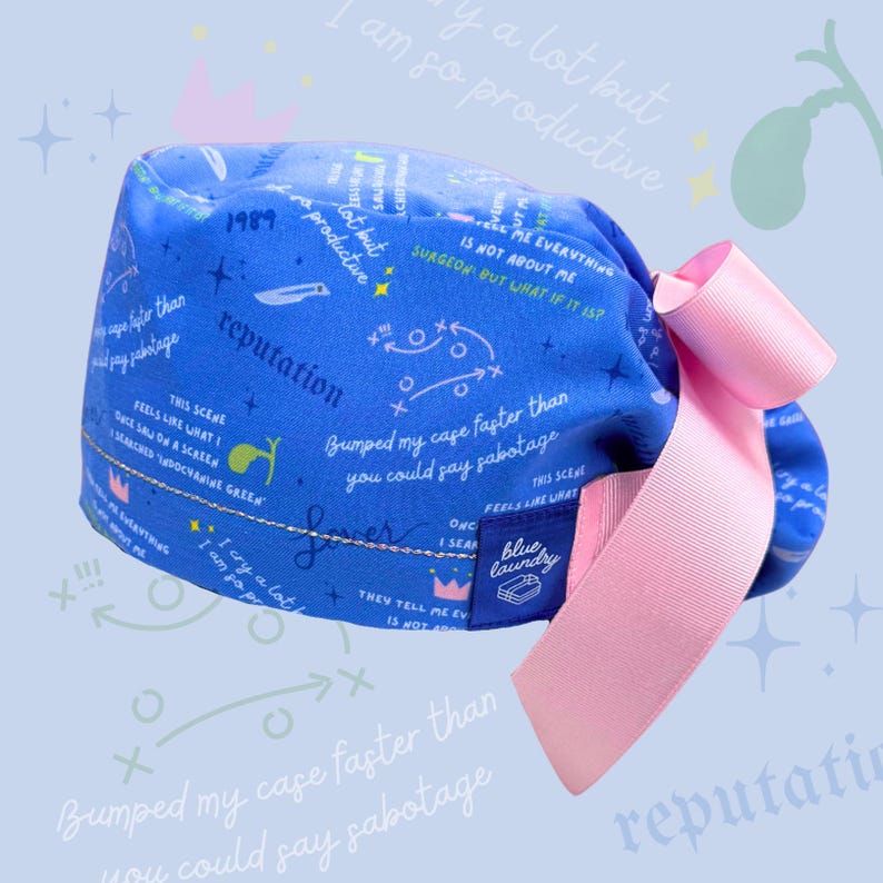 May include: Blue and white patterned surgical scrub hat with a pink ribbon. The hat has text that says "I am so productive" and "Bumped my case faster than you could say sabotage". The hat also has a blue and white label that says "Blue Laundry".