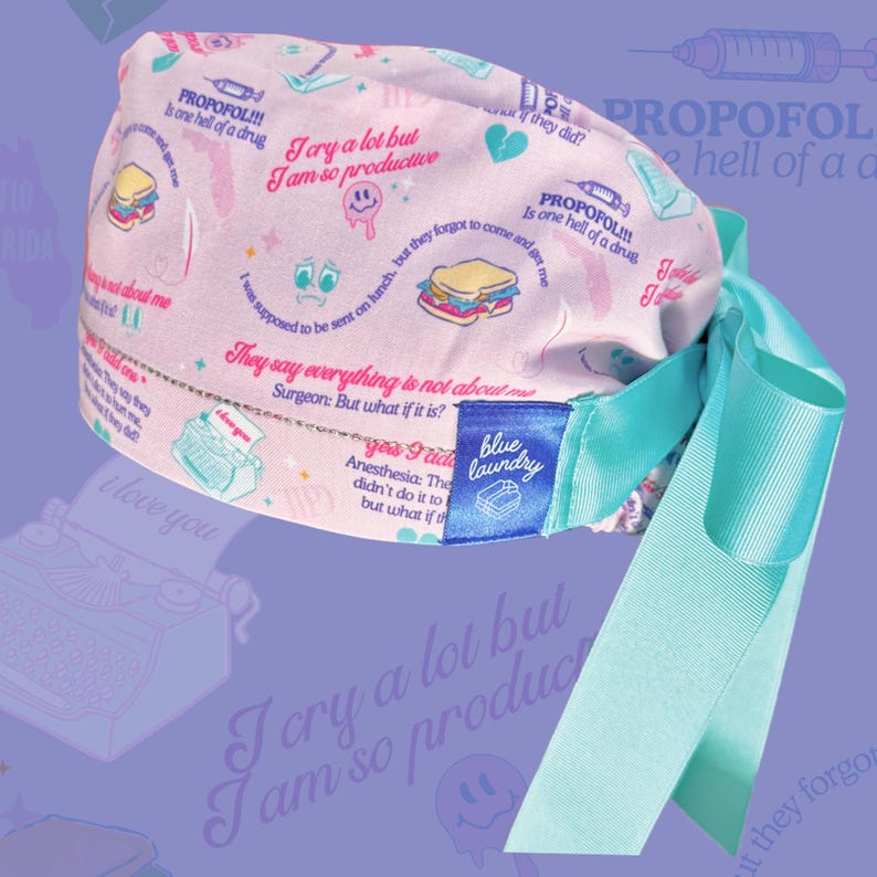Puede incluir: Un gorro quir&uacute;rgico rosa claro con una cinta turquesa. El gorro est&aacute; estampado con ilustraciones y frases de tem&aacute;tica m&eacute;dica en rosa y turquesa. Una etiqueta azul con la inscripci&oacute;n "blue laundry" est&aacute; cosida en el lateral.