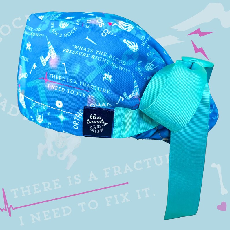 May include: Blue surgical scrub hat with a turquoise ribbon. The hat has a white print of medical tools, bones, and text that says "What's the blood pressure right now?" and "There is a fracture. I need to fix it." The hat also has a blue label that says "Blue Laundry" and "Ortho Quad".