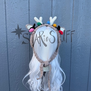 May include: A crocheted reindeer antler headband with colourful lights and a brown tie. The headband features white antlers, black and tan ears, and a string of colourful lights. The text "STAR to STUFF" is visible on the image.