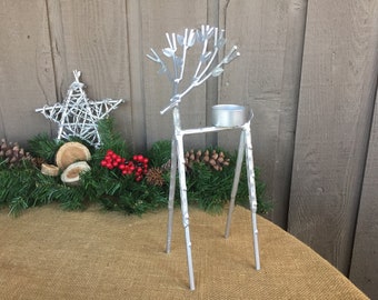 May include: Silver metal reindeer candle holder with a small round candle holder on top. The reindeer is standing on a brown burlap surface.