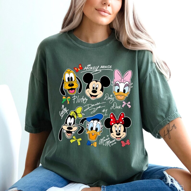 May include: Green t-shirt featuring Mickey Mouse and friends. The design includes Pluto, Mickey, Daisy Duck, Donald Duck, Goofy, and Minnie Mouse. The text "Mickey Mouse" is above the characters.