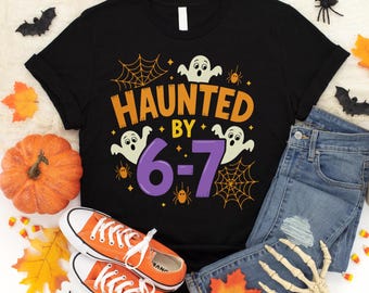 May include: Black t-shirt with the text "HAUNTED BY 6-7" in orange and purple, featuring ghost and spider graphics. The shirt is paired with orange sneakers, blue jeans, and Halloween decorations like a pumpkin and leaves.