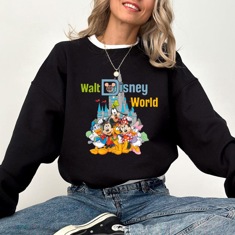 Puede incluir: Sudadera negra con el texto "Walt Disney World" en verde, azul y amarillo. El dise&ntilde;o incluye personajes de Disney como Mickey Mouse, el Pato Donald y Goofy frente a un castillo.