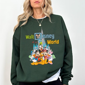 Puede incluir: Sudadera verde oscuro con el texto "Walt Disney World" y un gr&aacute;fico de personajes de Disney y el castillo de Cenicienta. La sudadera tiene cuello redondo y mangas largas. El gr&aacute;fico incluye Mickey Mouse, Donald Duck, Goofy y Minnie Mouse.