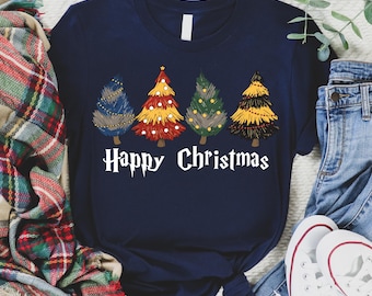 Op de afbeelding: Marineblauwe t-shirt met vier gestileerde kerstbomen in blauw, rood, groen en geel, elk met unieke decoratieve elementen. De woorden "Happy Christmas" staan eronder in het wit gedrukt. Het shirt wordt getoond met een jeans en sneakers.
