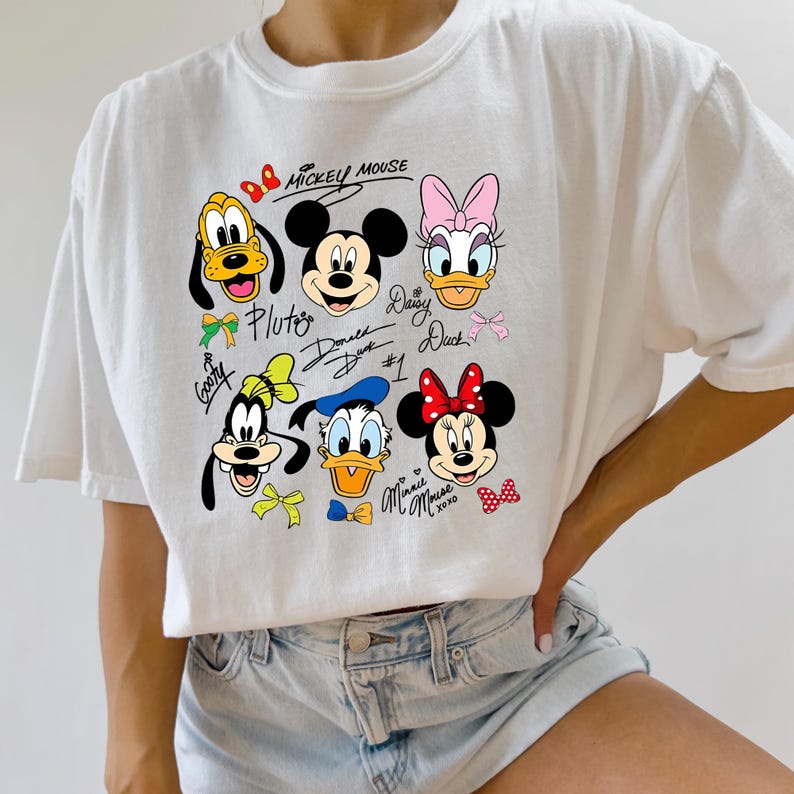 May include: White t-shirt featuring cartoon illustrations of Mickey Mouse, Minnie Mouse, Donald Duck, Daisy Duck, Pluto, and Goofy. The shirt includes the text "Mickey Mouse" and character names in a playful design.