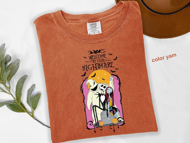 Puede incluir: Una camiseta color &ntilde;ame con un gr&aacute;fico de "Pesadilla antes de Navidad". El dise&ntilde;o incluye a Jack Skellington, Sally y Oogie Boogie, con el texto "Welcome to our Nightmare" y murci&eacute;lagos.