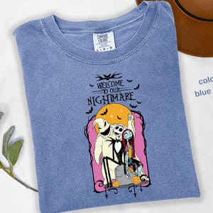 Puede incluir: Camiseta azul vaquero con un gr&aacute;fico de "Pesadilla antes de Navidad". El dise&ntilde;o incluye a Jack Skellington, Sally y Oogie Boogie, con el texto "Welcome to our Nightmare". Tambi&eacute;n se incluyen murci&eacute;lagos y calabazas.