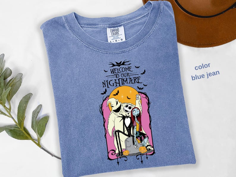 Puede incluir: Camiseta azul vaquero con un gr&aacute;fico de "Pesadilla antes de Navidad". El dise&ntilde;o incluye a Jack Skellington, Sally y Oogie Boogie, con el texto "Welcome to our Nightmare". Tambi&eacute;n se incluyen murci&eacute;lagos y calabazas.