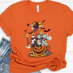 K&ouml;nnte beinhalten: Orangefarbenes T-Shirt mit einem Halloween-Motiv. Das Design zeigt Charaktere aus Nightmare Before Christmas, einen K&uuml;rbis, Flederm&auml;use und eine Spinne. Das Shirt besteht aus einem weichen Material und hat kurze &Auml;rmel.