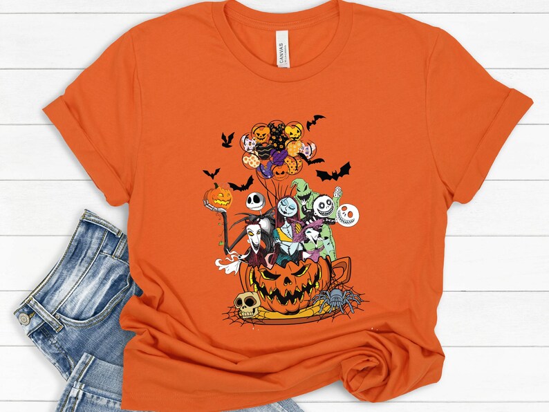 K&ouml;nnte beinhalten: Orangefarbenes T-Shirt mit einem Halloween-Motiv. Das Design zeigt Charaktere aus Nightmare Before Christmas, einen K&uuml;rbis, Flederm&auml;use und eine Spinne. Das Shirt besteht aus einem weichen Material und hat kurze &Auml;rmel.