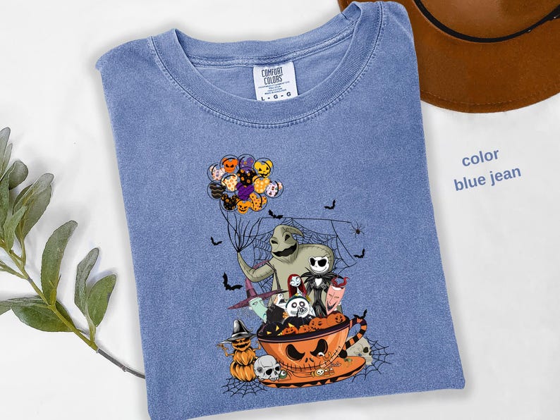 Pode incluir: Camiseta azul jeans com um gr&aacute;fico tem&aacute;tico de Halloween. O design inclui personagens de O Estranho Mundo de Jack, morcegos e uma ab&oacute;bora. A camisa tem gola redonda e mangas curtas. O texto "color blue jean" &eacute; vis&iacute;vel.