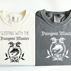 May include: Two t-shirts with a dragon and dice graphic and the text "Sleeping with the Dungeon Master" and "Dungeon Master".