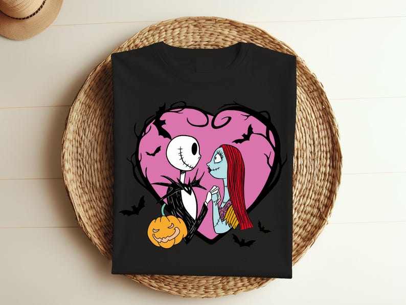 May include: Black t-shirt with a design of Jack Skellington and Sally from The Nightmare Before Christmas, framed by a pink heart and bats. A jack-o'-lantern is also included. The design has a romantic and spooky theme.