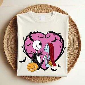 May include: Off-white t-shirt with a graphic of Jack Skellington and Sally from The Nightmare Before Christmas, within a pink heart-shaped frame with bats. A jack-o'-lantern is at the bottom. The design is on a woven basket.
