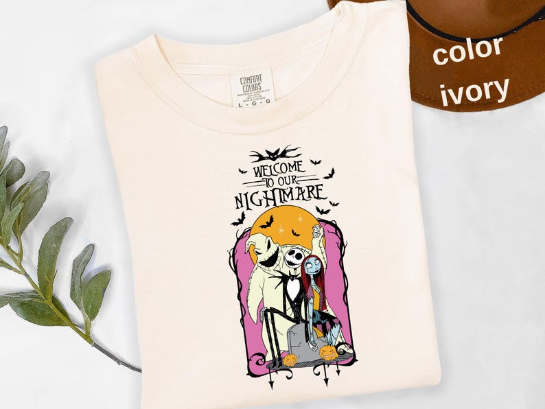 Puede incluir: Camiseta color marfil con un gr&aacute;fico de "Pesadilla antes de Navidad". El dise&ntilde;o incluye a Jack Skellington, Sally y Oogie Boogie frente a una luna llena, con el texto "WELCOME TO OUR NIGHTMARE."