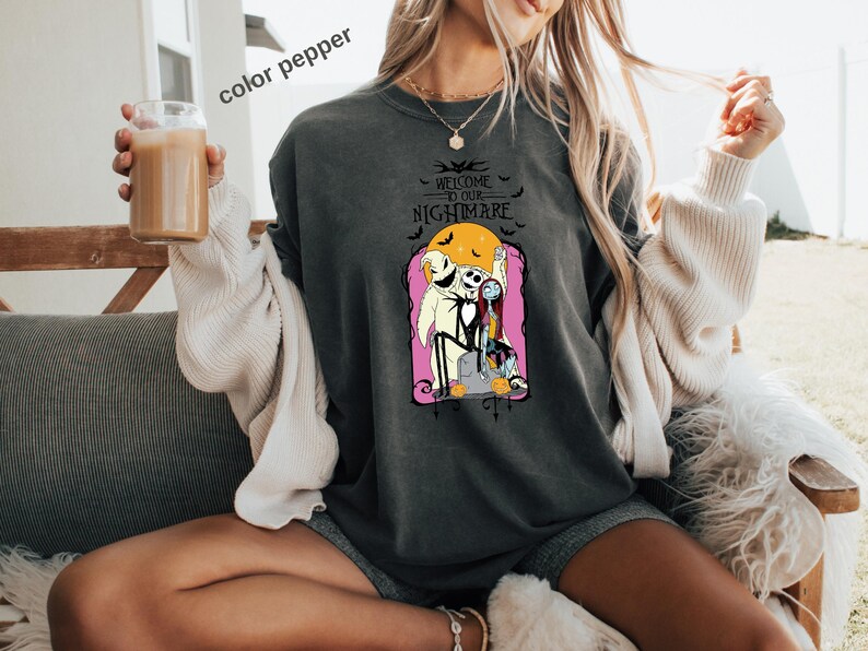 Puede incluir: Sudadera gris oscuro con un gr&aacute;fico de Jack Skellington y Sally de The Nightmare Before Christmas, con el texto "Welcome to our Nightmare". El dise&ntilde;o incluye una luna llena y murci&eacute;lagos.