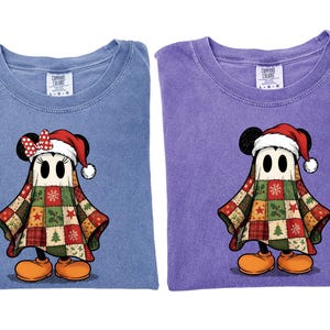 May include: Two Comfort Colors t-shirts, one blue and one purple, each featuring a cartoon ghost dressed as Mickey and Minnie Mouse in Christmas attire. The ghosts wear Santa hats and patchwork quilt capes.