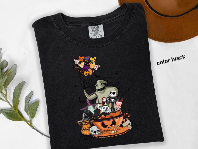 Pode incluir: Camiseta preta com um gr&aacute;fico tem&aacute;tico de Halloween. O design inclui personagens como Oogie Boogie e Jack Skellington, e uma tigela de ab&oacute;bora. Um grupo de bal&otilde;es de ursinhos de pel&uacute;cia flutua acima dos personagens. As palavras "color black" s&atilde;o vis&iacute;veis.