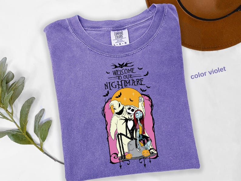 Puede incluir: Camiseta violeta Comfort Colors con un gr&aacute;fico de "Pesadilla antes de Navidad". El dise&ntilde;o incluye a Jack Skellington, Sally y Oogie Boogie con el texto "Welcome to our Nightmare" y murci&eacute;lagos.