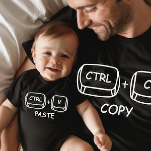 May include: A black onesie with the text "CTRL + V PASTE" and a black t-shirt with the text "CTRL + C COPY". The baby and adult are smiling. The theme is a computer keyboard.