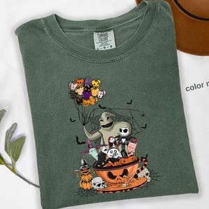 Pode incluir: Camiseta verde com um gr&aacute;fico tem&aacute;tico de Halloween. O design apresenta personagens de O Estranho Mundo de Jack, incluindo Jack Skellington, Oogie Boogie e Zero. A camisa tamb&eacute;m tem uma ab&oacute;bora, morcegos e bal&otilde;es.