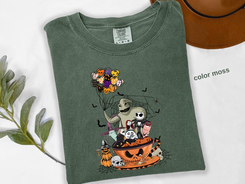Pode incluir: Camiseta verde com um gr&aacute;fico tem&aacute;tico de Halloween. O design apresenta personagens de O Estranho Mundo de Jack, incluindo Jack Skellington, Oogie Boogie e Zero. A camisa tamb&eacute;m tem uma ab&oacute;bora, morcegos e bal&otilde;es.