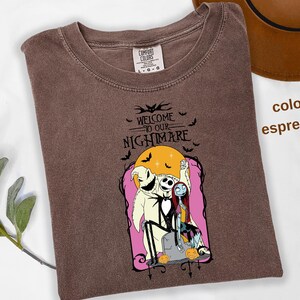 Puede incluir: Camiseta color espresso con un gr&aacute;fico de "Pesadilla antes de Navidad". El dise&ntilde;o incluye a Jack Skellington, Sally y Oogie Boogie, con el texto "Welcome to our Nightmare". Murci&eacute;lagos y calabazas completan el tema espeluznante.