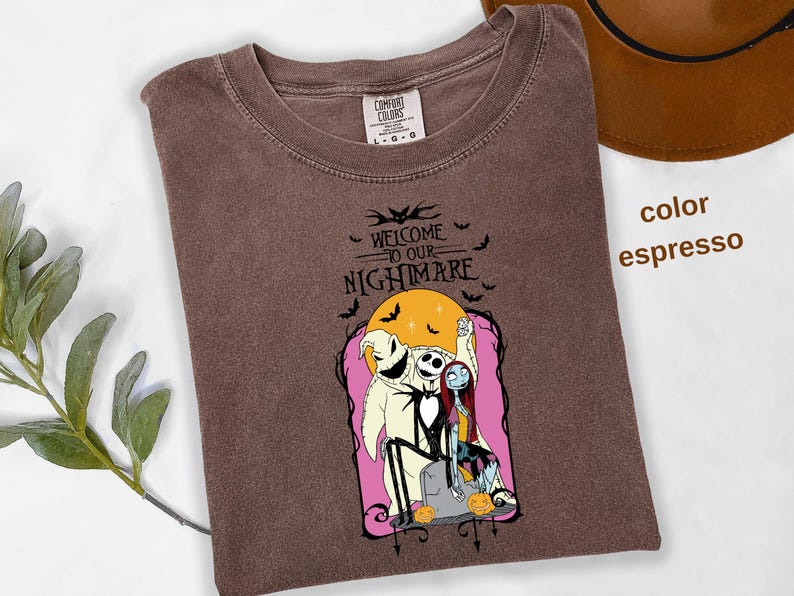 Puede incluir: Camiseta color espresso con un gr&aacute;fico de "Pesadilla antes de Navidad". El dise&ntilde;o incluye a Jack Skellington, Sally y Oogie Boogie, con el texto "Welcome to our Nightmare". Murci&eacute;lagos y calabazas completan el tema espeluznante.