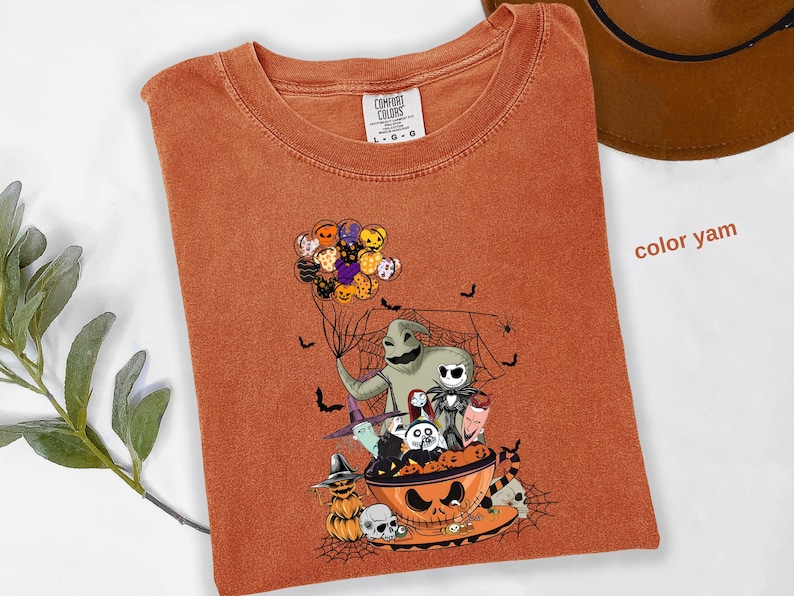 Pode incluir: Camiseta laranja Comfort Colors com um gr&aacute;fico tem&aacute;tico de Halloween. O design apresenta personagens de O Estranho Mundo de Jack, incluindo Jack Skellington e Oogie Boogie. A camisa tem gola redonda e mangas curtas.