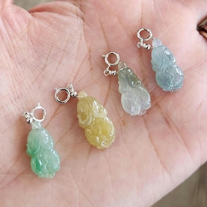 Puede incluir: Cuatro pequeños colgantes tallados en forma de calabaza, hechos de piedra translúcida en tonos verde, amarillo y azul pálido. Cada colgante cuenta con una anilla de metal plateado en la parte superior para facilitar su sujeción a cadenas.