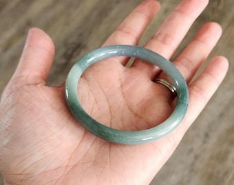 May include: A jade bangle bracelet with a green and white color gradient. The bangle is smooth and polished.
