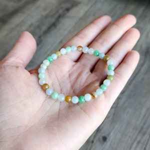 May include: A jade bracelet with green, white, and brown beads. The bracelet is made of natural jade and is a beautiful and unique piece of jewelry.